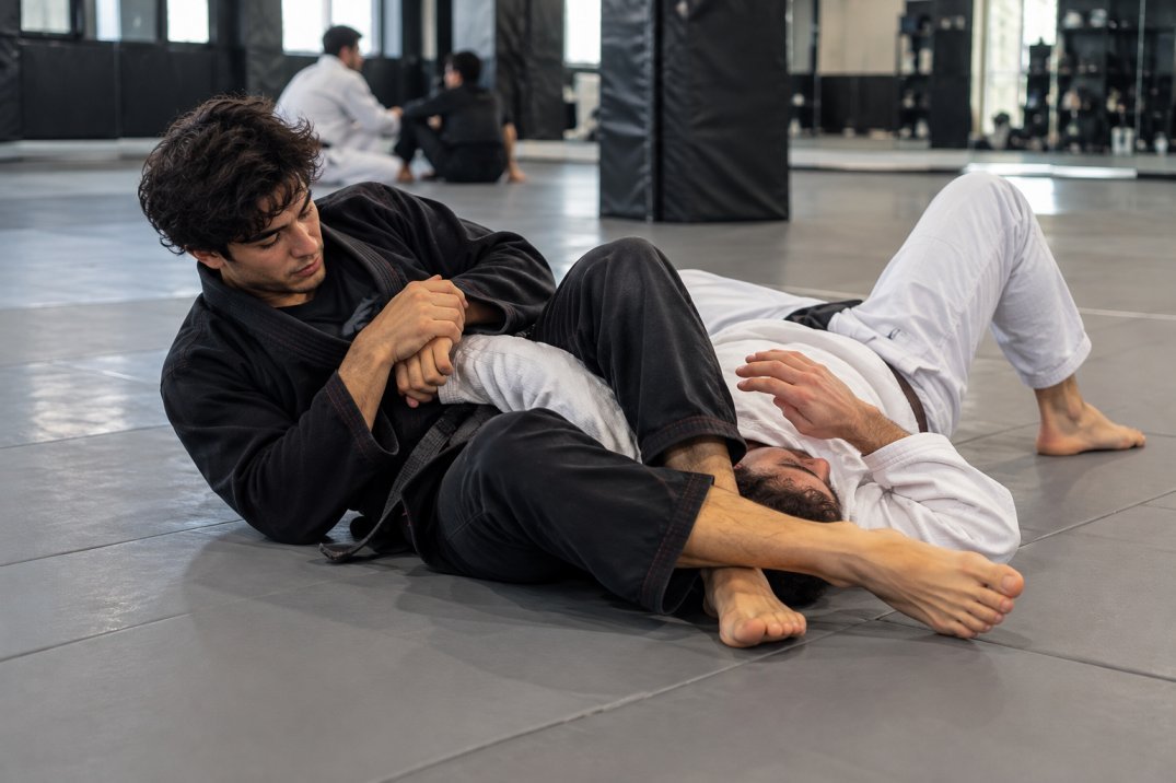 Beginners practising a controlled BJJ armbar training drill on clean grappling mats