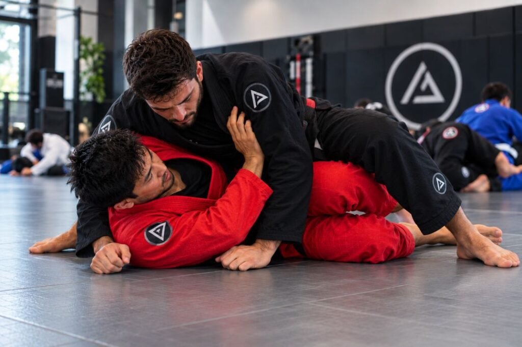 Brazilian Jiu-Jitsu athletes in black and red gis practicing side control and defensive framing on gym mats